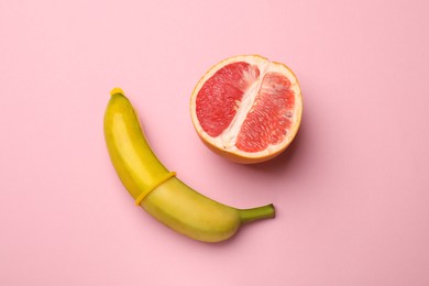 Photo of Sex education. Banana with condom and grapefruit on pink background, top view