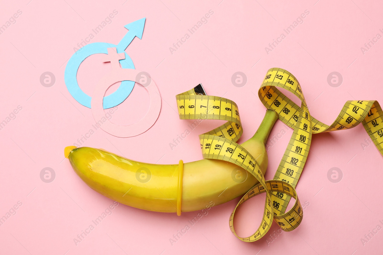 Sex education. Banana with condom, measuring tape, paper female and male gender symbols on pink background, flat lay Photo of Sex education. Banana with condom, measuring tape, paper female and male gender symbols on pink background, flat lay