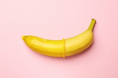 Photo of Sex education. Banana with condom on pink background, top view