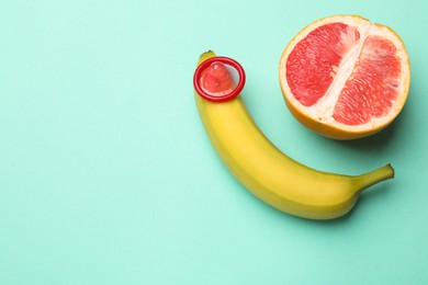 Photo of Sex education. Banana with condom and grapefruit on turquoise background, top view. Space for text