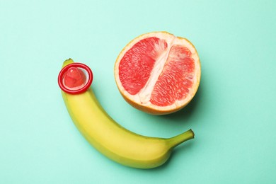 Photo of Sex education. Banana with condom and grapefruit on turquoise background, top view