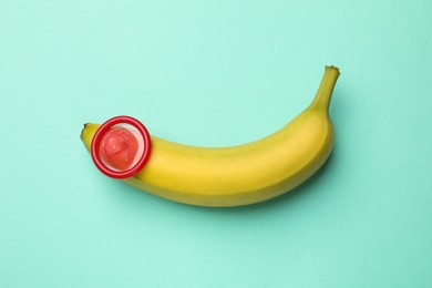 Photo of Sex education. Banana with condom on turquoise background, top view