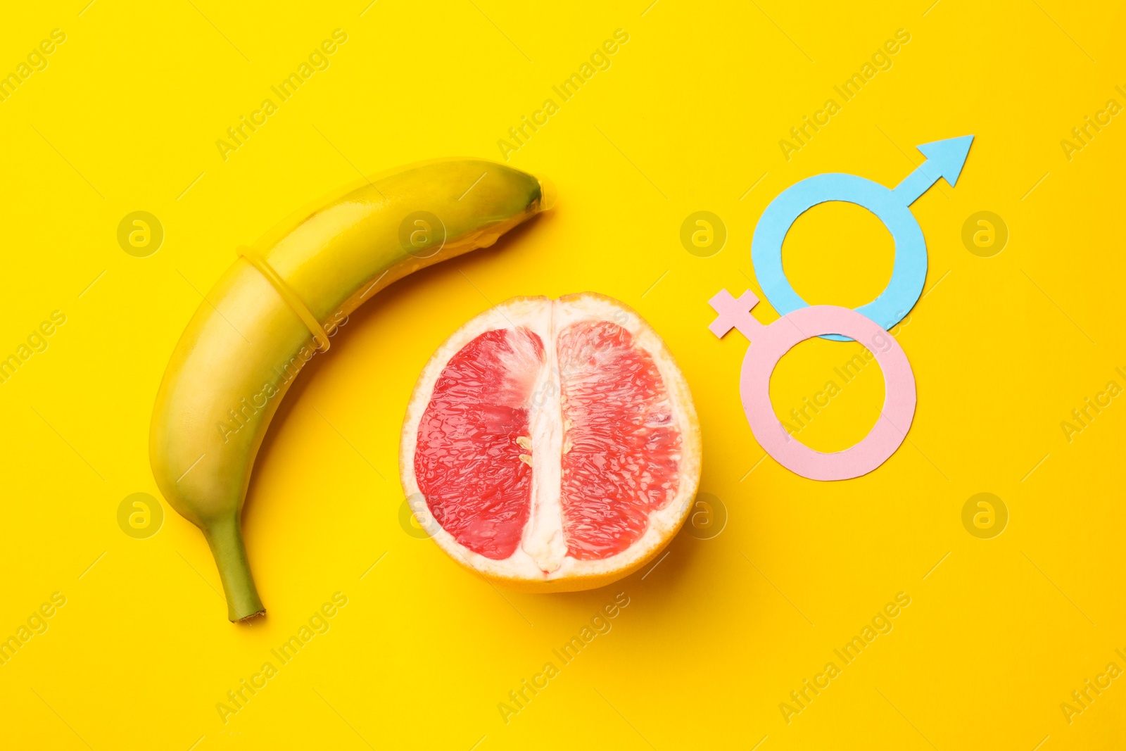 Sex education. Banana with condom, grapefruit, paper female and male gender symbols on yellow background, flat lay Photo of Sex education. Banana with condom, grapefruit, paper female and male gender symbols on yellow background, flat lay