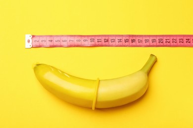 Photo of Sex education. Banana with condom and measuring tape on yellow background, top view