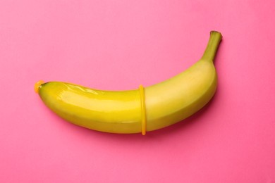 Photo of Sex education. Banana with condom on pink background, top view