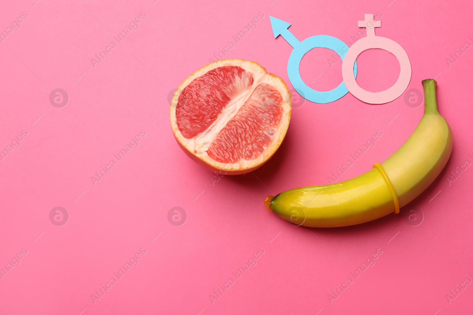 Sex education. Banana with condom, grapefruit, paper female and male gender symbols on pink background, flat lay. Space for text Photo of Sex education. Banana with condom, grapefruit, paper female and male gender symbols on pink background, flat lay. Space for text