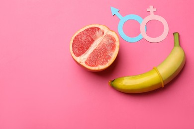 Photo of Sex education. Banana with condom, grapefruit, paper female and male gender symbols on pink background, flat lay. Space for text