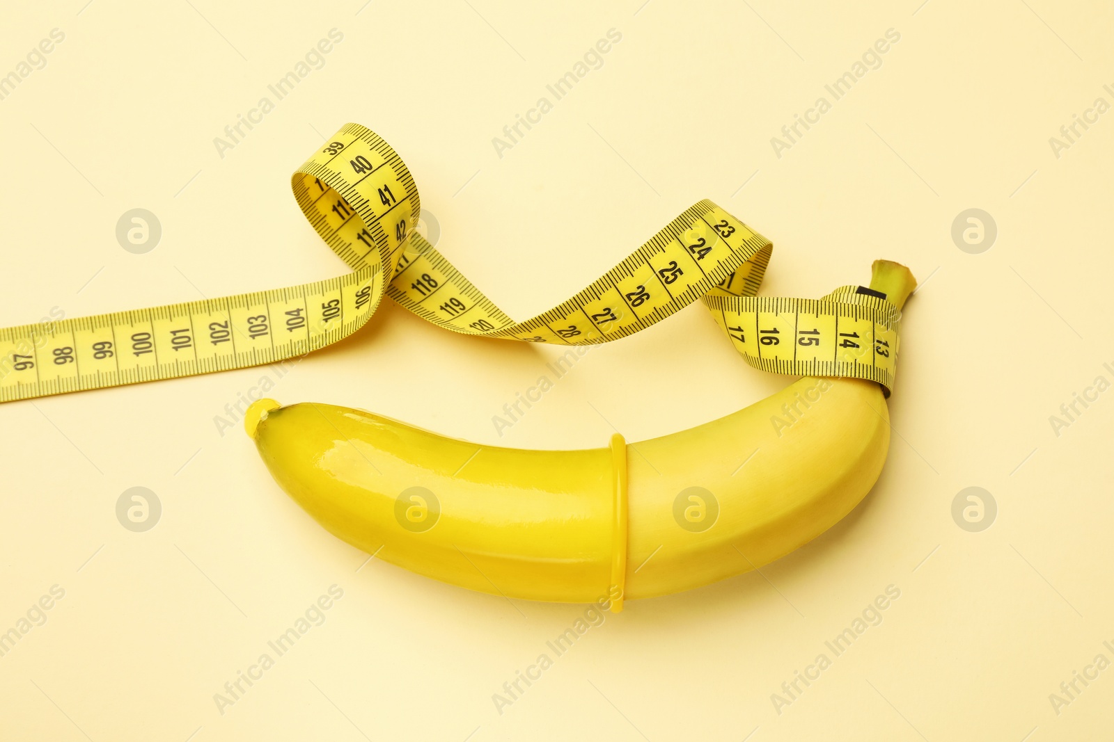Sex education. Banana with condom and measuring tape on beige background, top view Photo of Sex education. Banana with condom and measuring tape on beige background, top view