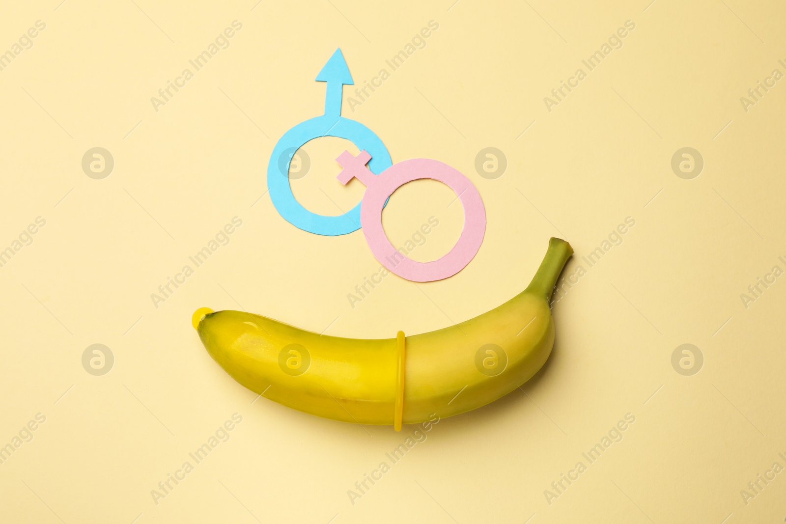 Sex education. Banana with condom, paper female and male gender symbols on beige background, flat lay Photo of Sex education. Banana with condom, paper female and male gender symbols on beige background, flat lay