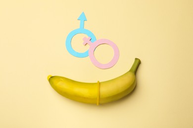 Photo of Sex education. Banana with condom, paper female and male gender symbols on beige background, flat lay