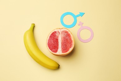 Photo of Sex education. Banana, grapefruit, paper female and male gender symbols on beige background, flat lay