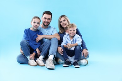 Photo of Happy parents and their children sitting on light blue background. Family