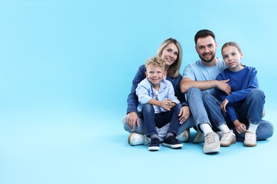 Photo of Happy parents and their children sitting on light blue background, space for text. Family