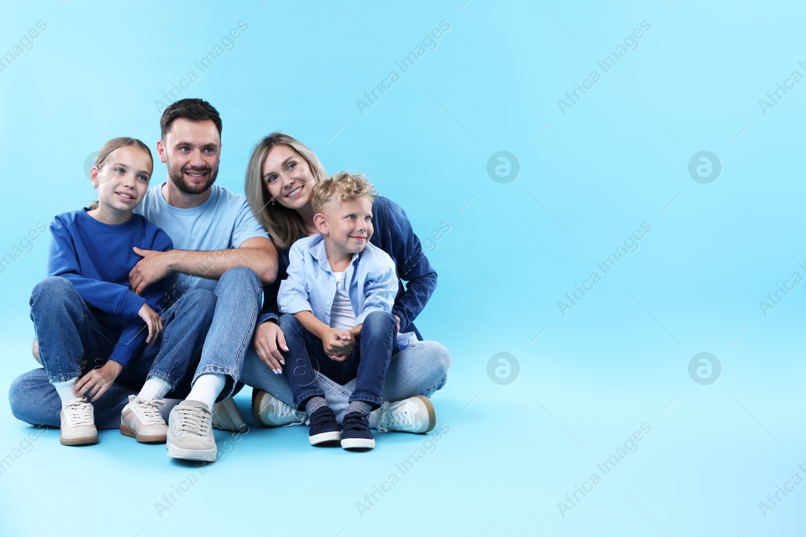 Happy parents and their children sitting on light blue background, space for text. Family Photo of Happy parents and their children sitting on light blue background, space for text. Family