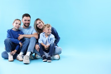 Photo of Happy parents and their children sitting on light blue background, space for text. Family