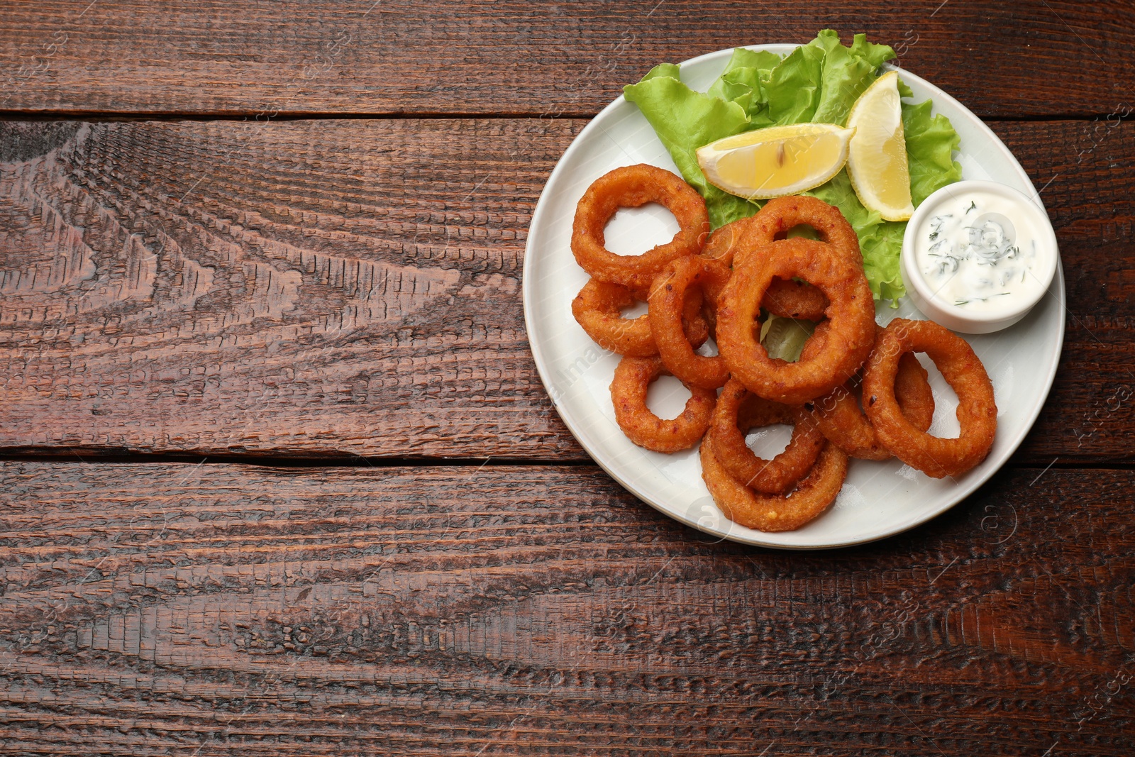 Fried squid rings, lemon, lettuce and sauce on wooden table, top view. Space for text Photo of Fried squid rings, lemon, lettuce and sauce on wooden table, top view. Space for text