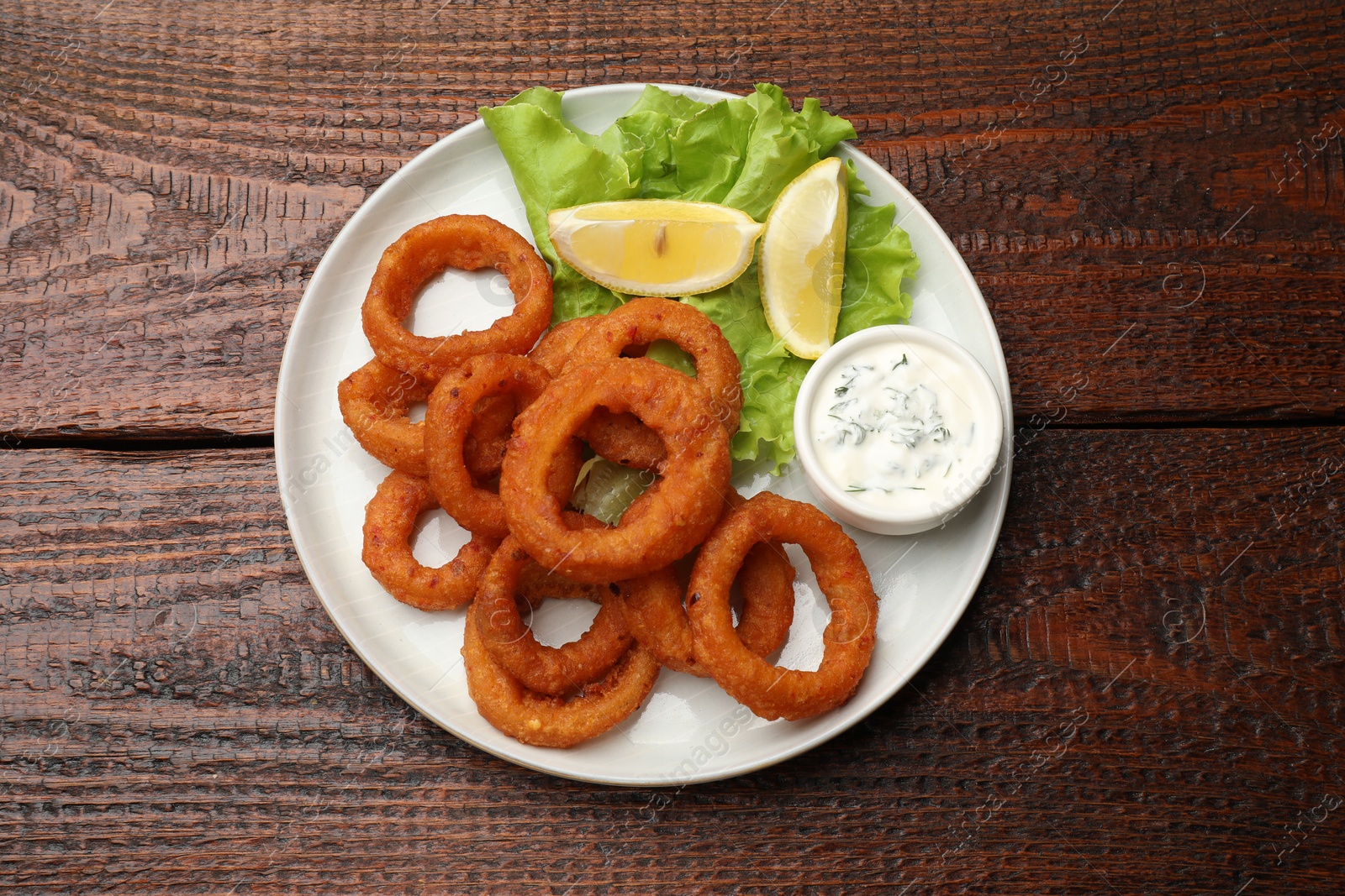Fried squid rings, lemon, lettuce and sauce on wooden table, top view Photo of Fried squid rings, lemon, lettuce and sauce on wooden table, top view