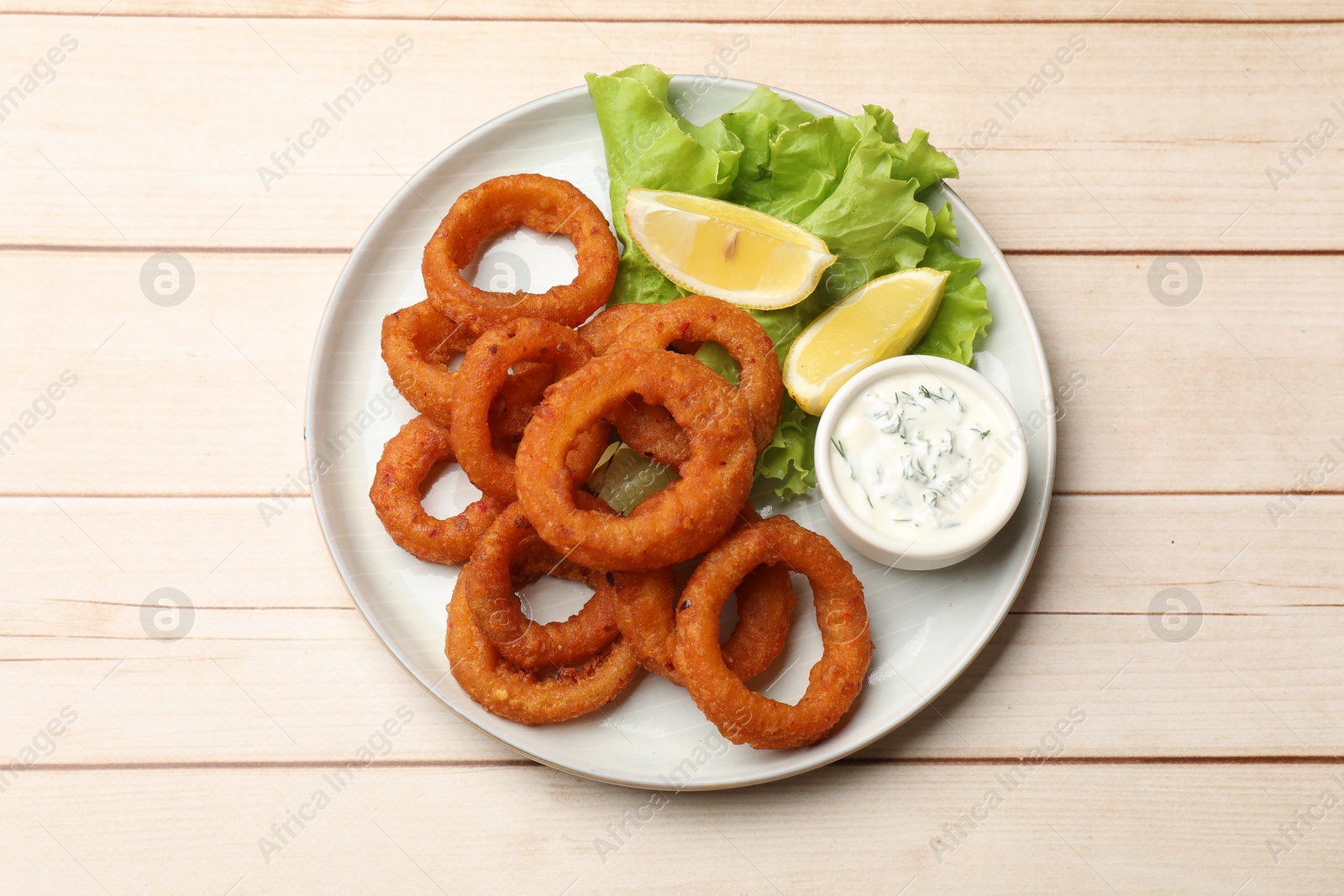 Fried squid rings, lemon, lettuce and sauce on light wooden table, top view Photo of Fried squid rings, lemon, lettuce and sauce on light wooden table, top view