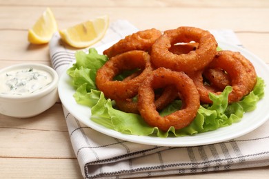 Photo of Fried squid rings, lemon, lettuce and sauce on light wooden table, closeup