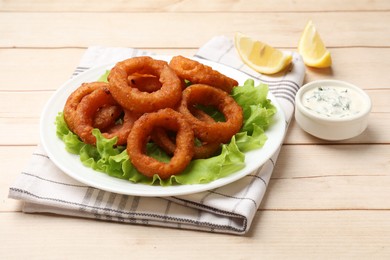 Photo of Fried squid rings, lemon, lettuce and sauce on light wooden table, closeup