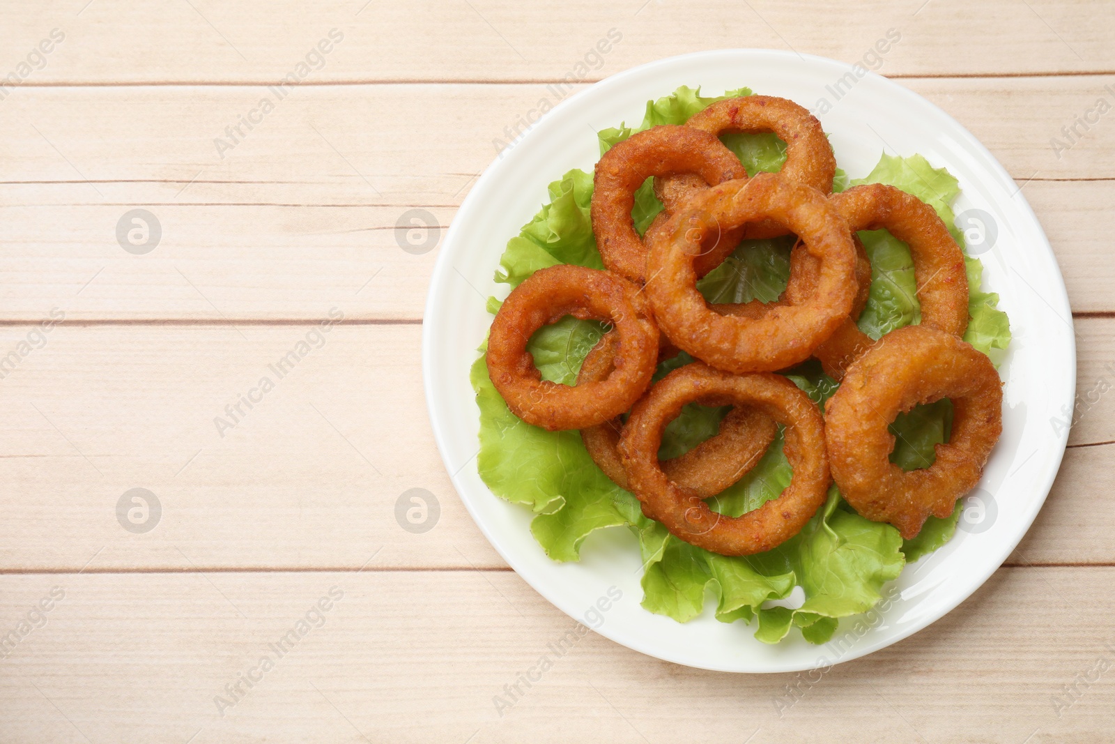 Photo of Fried squid rings and lettuce on light wooden table, top view. Space for text