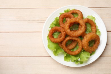 Photo of Fried squid rings and lettuce on light wooden table, top view. Space for text