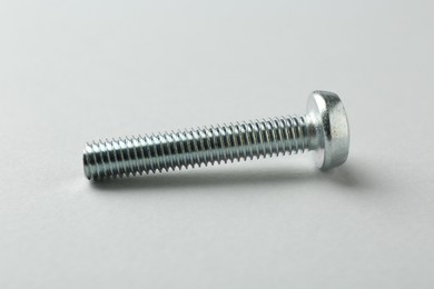 Photo of One metal bolt on light grey background, closeup. Hardware tool