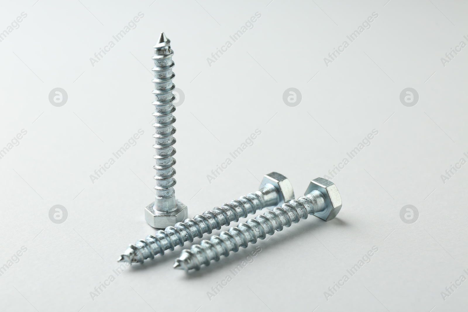 Three metal bolts on light grey background, closeup. Hardware tool Photo of Three metal bolts on light grey background, closeup. Hardware tool