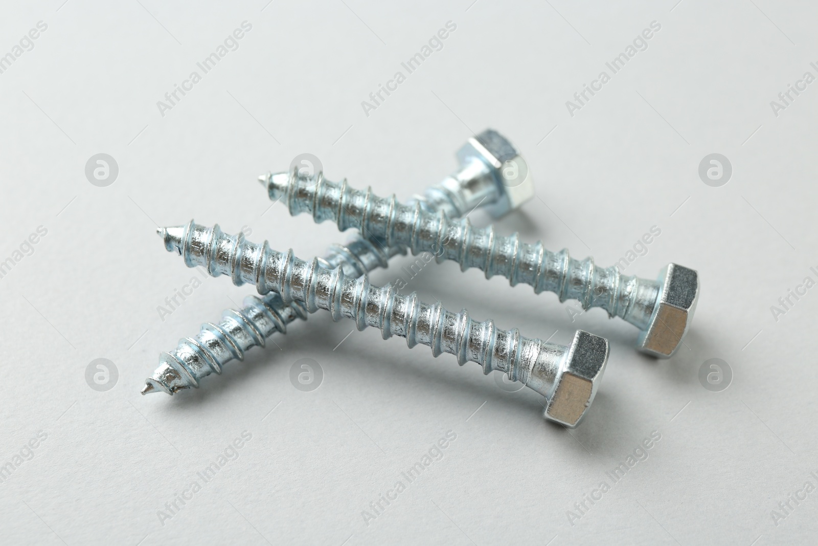 Photo of Three metal bolts on light grey background, closeup. Hardware tool