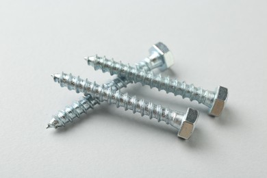Photo of Three metal bolts on light grey background, closeup. Hardware tool