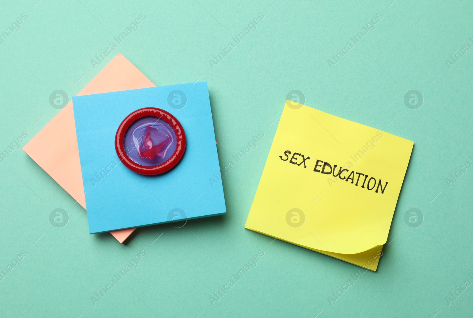 Photo of Sticky notes with words Sex Education and condom on turquoise background, flat lay