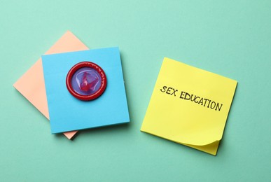 Photo of Sticky notes with words Sex Education and condom on turquoise background, flat lay