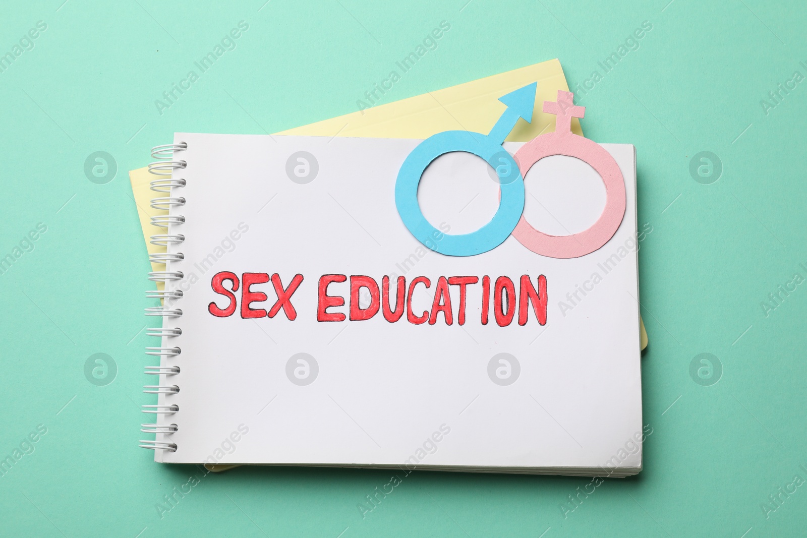 Photo of Notebook with words Sex Education and gender symbols on turquoise background, top view