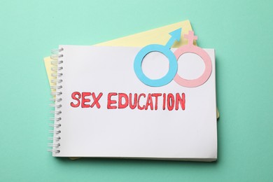 Photo of Notebook with words Sex Education and gender symbols on turquoise background, top view