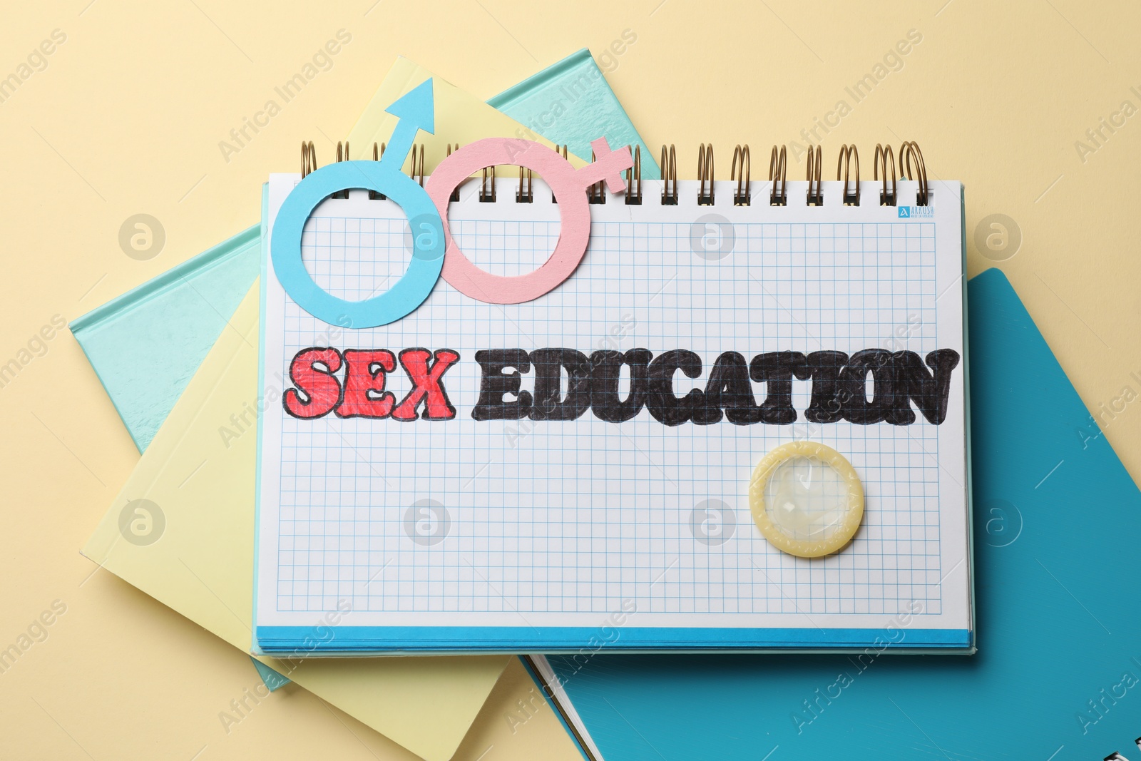 Photo of Notebook with words Sex Education, gender symbols, condom and notebooks on beige background, flat lay