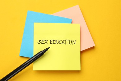 Photo of Sticky notes with words Sex Education and felt pen on yellow background, flat lay