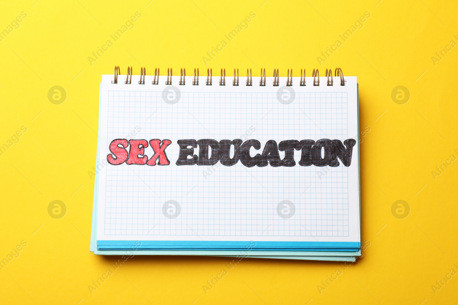 Photo of Notebook with words Sex Education on yellow background, top view