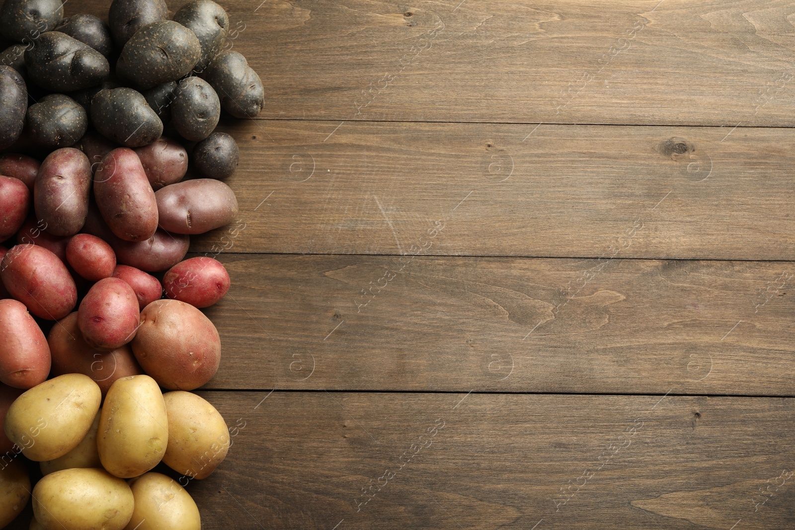 Photo of Different types of potatoes on wooden table, flat lay. Space for text