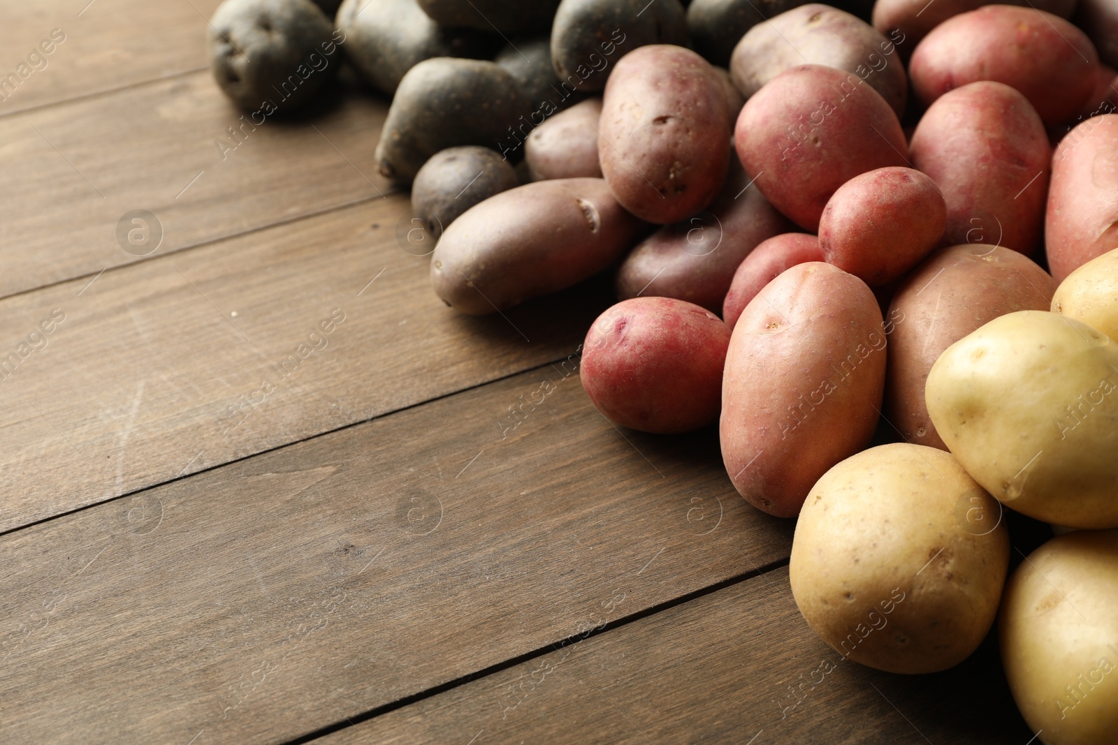 Photo of Different types of potatoes on wooden table, closeup. Space for text