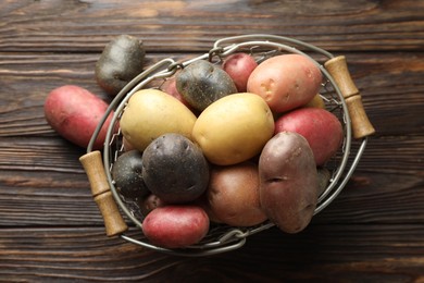 Photo of Different types of potatoes in metal basket on wooden table, top view