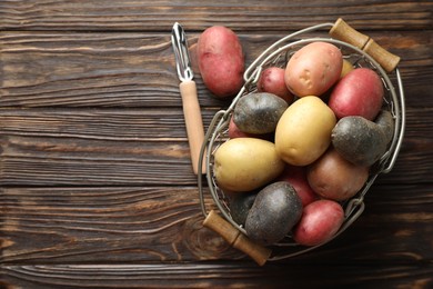 Photo of Different types of potatoes in metal basket and peeler on wooden table, flat lay. Space for text