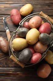 Photo of Different types of potatoes in metal basket and peeler on wooden table, flat lay