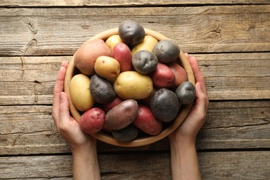 Photo of Woman with bowl of different types of potatoes at wooden table, top view