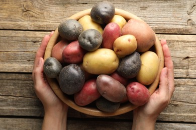 Photo of Woman with bowl of different types of potatoes at wooden table, top view