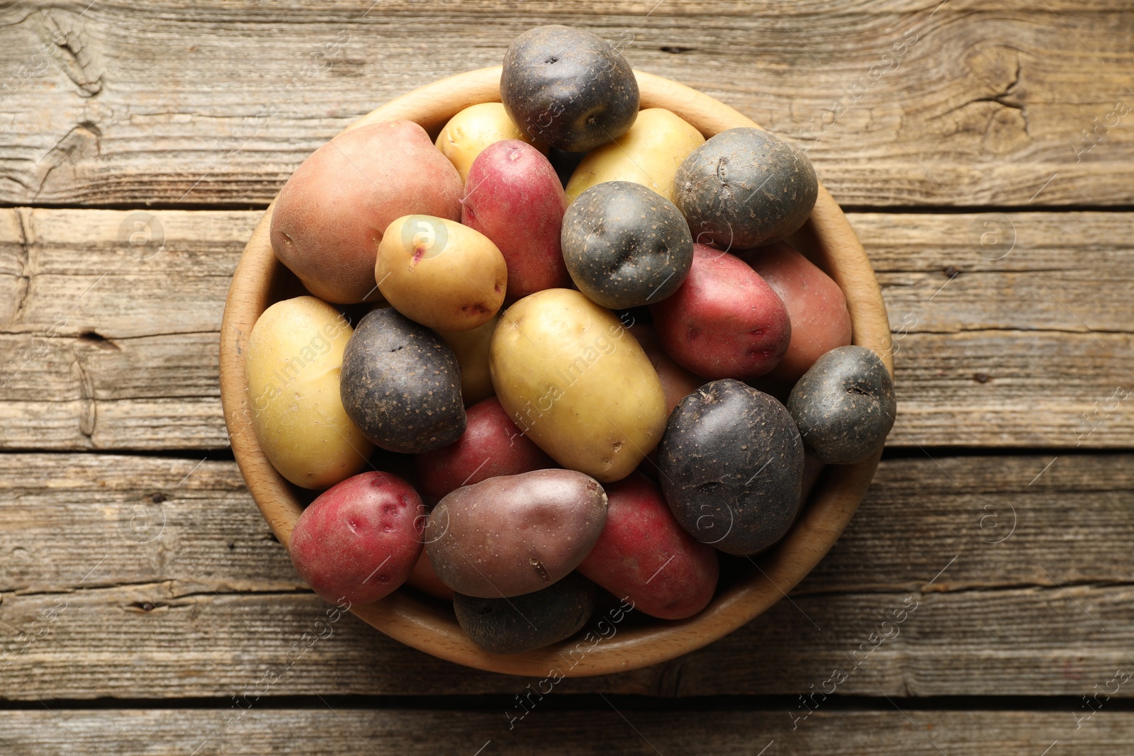 Photo of Different types of potatoes in bowl on wooden table, top view