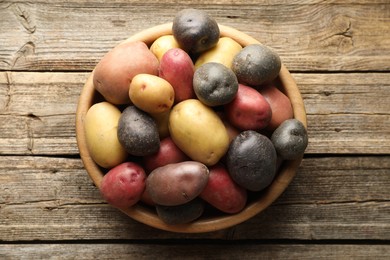 Photo of Different types of potatoes in bowl on wooden table, top view