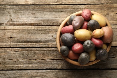 Photo of Different types of potatoes in bowl on wooden table, top view. Space for text