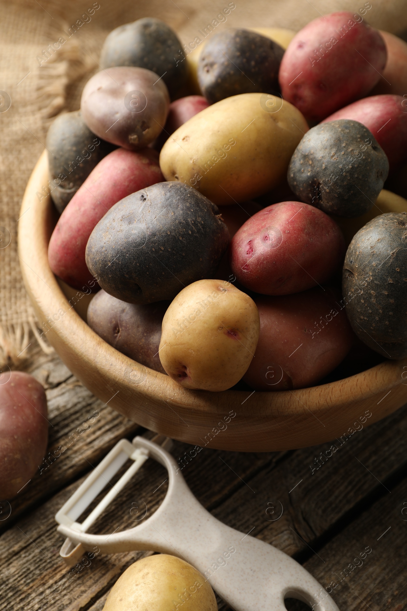 Different types of potatoes in bowl and peeler on wooden table, closeup Photo of Different types of potatoes in bowl and peeler on wooden table, closeup