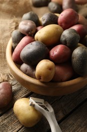 Photo of Different types of potatoes in bowl and peeler on wooden table, closeup