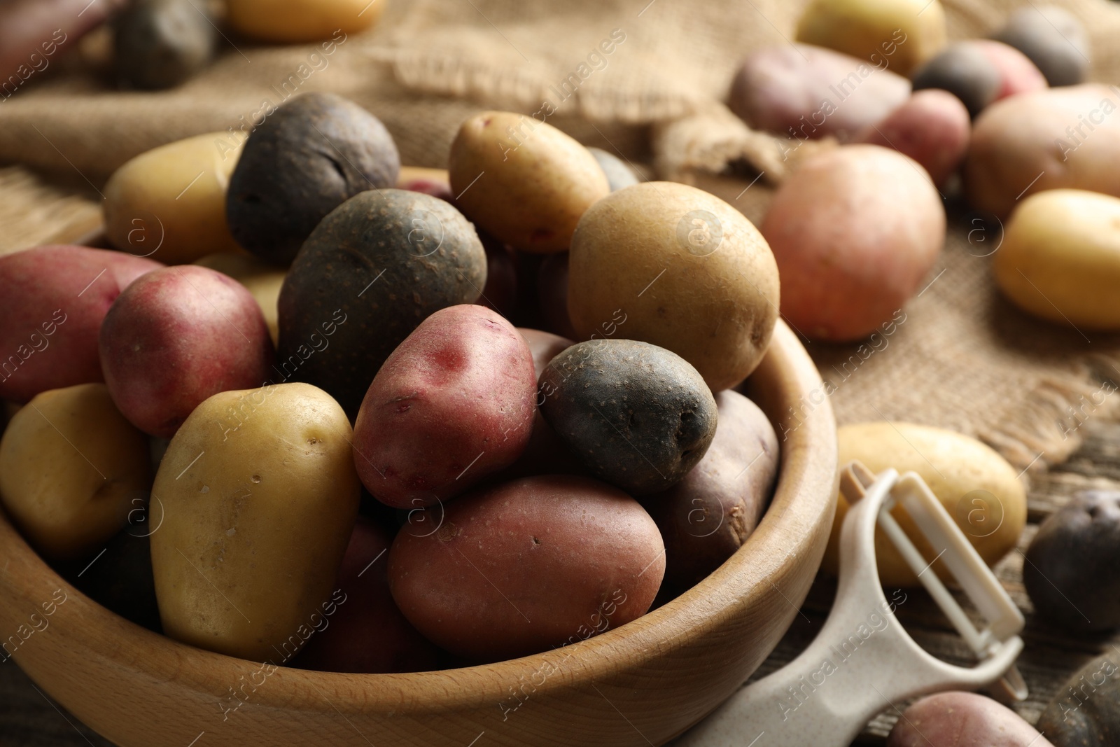 Photo of Different types of potatoes in bowl and peeler on table, closeup